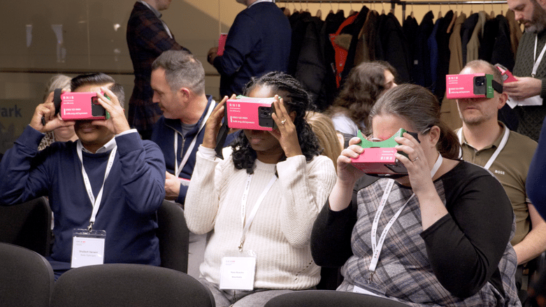 Group of attendees using RNIB-branded virtual reality headsets, seated in rows at a conference.